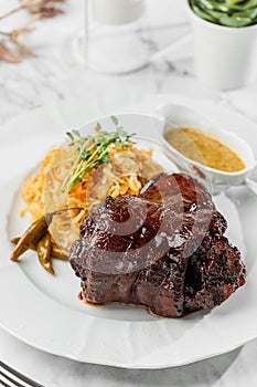 Tasty Baked Eisbein  pork knuckle , with salad and mustard at the white plate on light marble background. Healthy sea food, hard