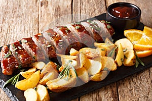 Tasty baked pork tenderloin in honey-orange glaze with potato wedges close-up on a plate. horizontal