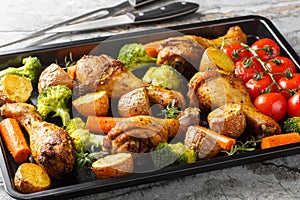 Tasty Baked ruddy chicken legs with potatoes, broccoli, tomato, carrot close-up on a baking sheet. Horizontal