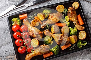 Tasty Baked ruddy chicken legs with potatoes, broccoli, tomato, carrot close-up on a baking sheet. Horizontal top view