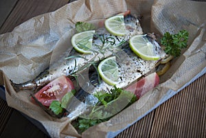 Tasty baked whole sea fishes on baking paper. Baked sea bream with lemon, herbs, tomatoes, spices on woode rustic background. Gril