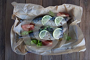 Tasty baked whole sea fishes on baking paper. Baked sea bream with lemon, herbs, tomatoes, spices on woode rustic background. Gril