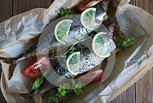 Tasty baked whole sea fishes on baking paper. Baked sea bream with lemon, herbs, tomatoes, spices on woode rustic background. Gril