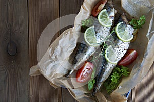 Tasty baked whole sea fishes on baking paper. Baked sea bream with lemon, herbs, tomatoes, spices on woode rustic background. Gril