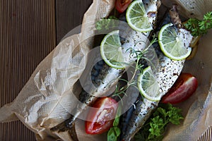 Tasty baked whole sea fishes on baking paper. Baked sea bream with lemon, herbs, tomatoes, spices on woode rustic background. Gril