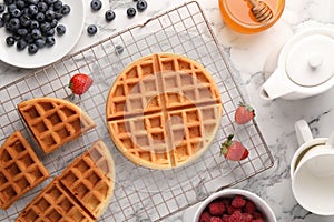 Tasty Belgian waffles with fresh berries and honey on white marble table, flat lay