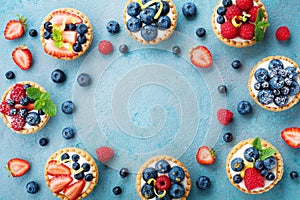 Tasty berry tartlets or cake with cream cheese and different berries around. Pastry dessert top view.
