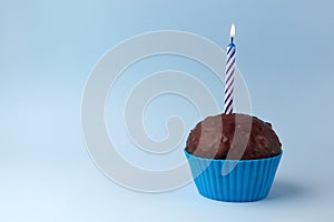 Tasty birthday cupcake with candle, on blue background, with free space