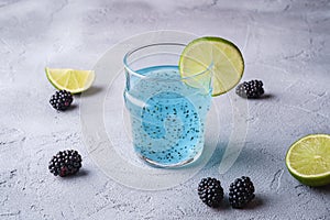 Tasty blue colored cocktail drink with basil chia seeds, citrus lime slice and blackberry in glass, healthy summer beverage