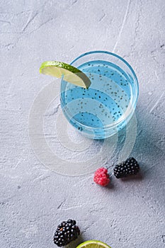 Tasty blue colored cocktail drink with basil chia seeds, citrus lime slice, raspberry and blackberry berries in glass