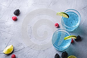 Tasty blue colored cocktail drink with basil chia seeds, citrus lime slice, raspberry and blackberry berries in two glass