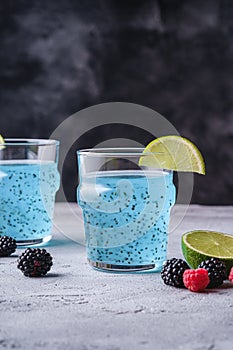 Tasty blue colored cocktail drink with basil chia seeds, citrus lime slice, raspberry and blackberry berries in two glass