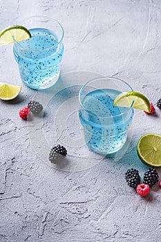 Tasty blue colored cocktail drink with basil chia seeds, citrus lime slice, raspberry and blackberry berries in two glass