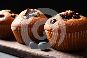 Tasty blueberry muffins on wooden board against black background