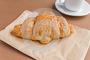 Tasty breackfast. French croissant served on white plate and cup of black coffee or espresso on brown background. Copy space