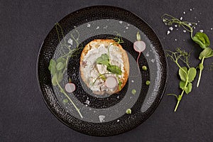 Tasty bread with cream cheese, peas and radish on black plate from above