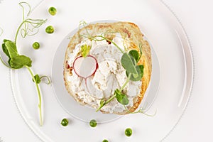 Tasty bread with cream cheese, peas and radish on white plate from above