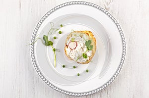 Tasty bread with cream cheese, peas and radish on white plate from above