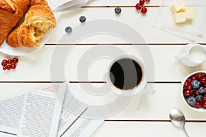 Tasty breakfast with coffee, berries, croissant on the white wooden table, top view