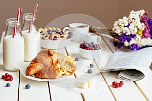 Tasty breakfast with croissant, oat flakes, berries and milk on the white wooden table