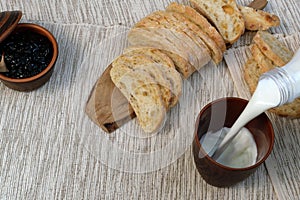 Tasty breakfast. Fresh bread with jam and milk. Milk is poured into a cup. Toast with fruit jam on napkin. Balanced food. Rustic