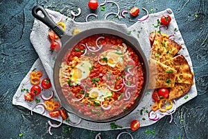 Tasty Breakfast Shakshuka in a Iron Pan. Fried eggs with tomatoes, red, yellow peppers, onion, parsley, Pita bread and