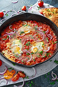 Tasty Breakfast Shakshuka in a Iron Pan. Fried eggs with tomatoes, red, yellow peppers, onion, parsley, Pita bread and