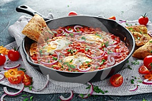 Tasty Breakfast Shakshuka in a Iron Pan. Fried eggs with tomatoes, red, yellow peppers, onion, parsley, Pita bread and