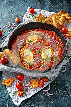 Tasty Breakfast Shakshuka in a Iron Pan. Fried eggs with tomatoes, red, yellow peppers, onion, parsley, Pita bread and