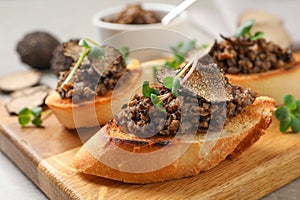 Tasty bruschettas with truffle paste on wooden board, closeup