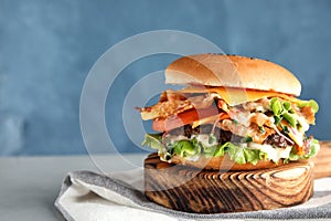 Tasty burger with bacon served on wooden board with tea-towel.