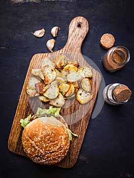 Tasty burger on cutting board with potato wedges with salt and pepper and garlic wooden rustic background top view close up