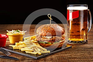 Tasty burger, french fries with sauce and glass of beer on black board