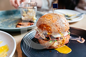 Tasty burger with fried egg and yolk served with fries in black plate on wooden table