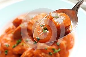 Tasty butter chicken in spoon over plate with meat