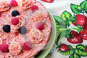 Tasty cake with strawberries, blackberries and colorful sprinkles on the green plate and colorful strawberry jam