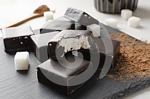 Tasty candies with chocolate and soft filling, cocoa powder and sugar on the dark surface