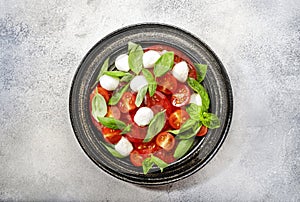 Tasty caprese salad with ripe red tomatoes and mozzarella cheese with fresh green basil leaves. Italian food. Top view