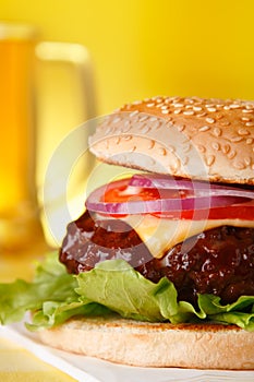 Tasty cheeseburger with pint of beer on background