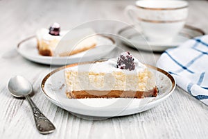 Tasty cheesecake with blackberry on a plate laying on a white wooden table with another cake and cup of coffee or tea on backgroun