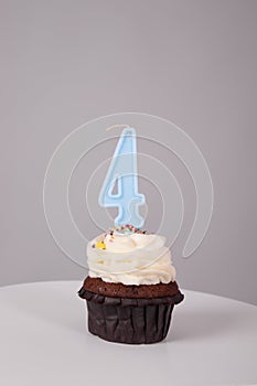 tasty chocolate cupcake with white topping cream and candle in shape of number four 4. on a white stand on a gray