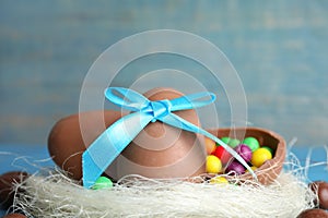 Tasty chocolate eggs with colorful candies in decorative nest against light blue background, closeup