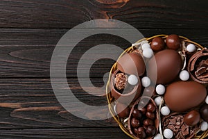 Tasty chocolate eggs and sweets in wicker basket on wooden table, top view. Space for text