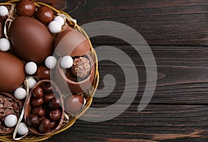 Tasty chocolate eggs and sweets in wicker basket on wooden table, top view. Space for text