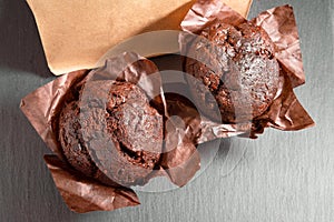 Tasty chocolate muffin cakes in baked paper on black background