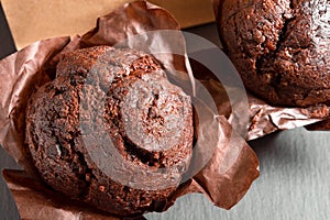 Tasty chocolate muffins in baked paper on black background, close-up