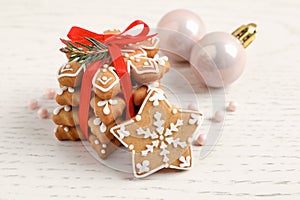 Tasty Christmas cookies tied with red ribbon and festive decor on beige wooden table, closeup