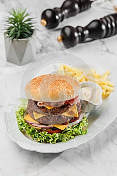 Tasty classic beef burger with french fries and sauce at the white plate on light marble background. Healthy sea food, hard light