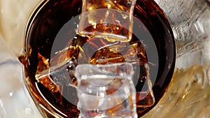 Tasty cola with bubbles is poured into a glass with ice cubes on a table. Concept of drinking coke or soda, relax and having fun