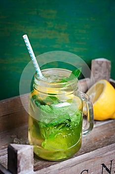 Tasty colorful drink with cold green tea, mint and lemon in a glass jar on a vintage background